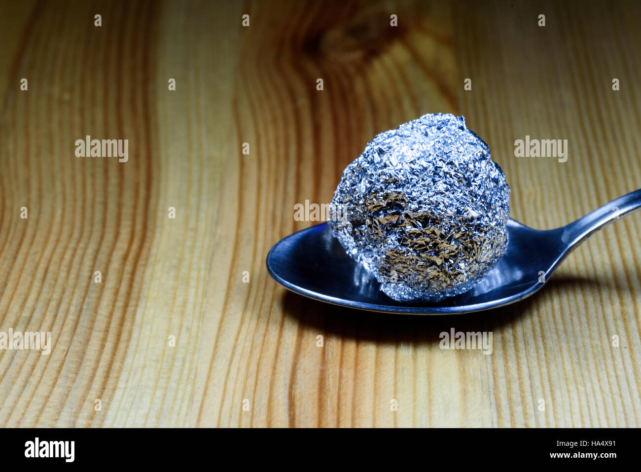 Ball des Heroins eingewickelt in Alufolie Ball ruht auf einem Silber Teelöffel auf eine hölzerne strukturierte Oberfläche. Stockfoto