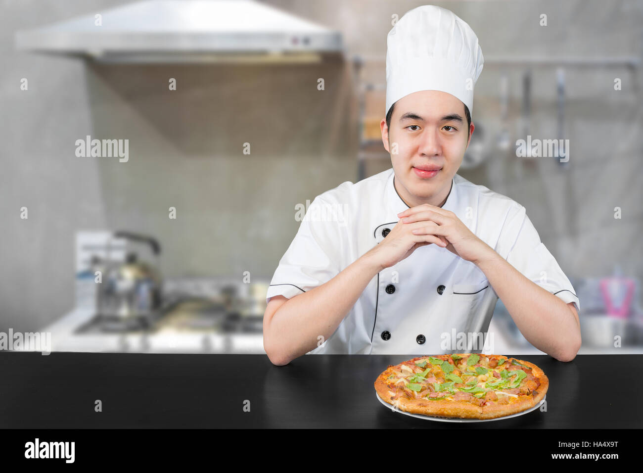 Asiatische junge Mann Chef in weiße uniform bietet Ihnen leckere Pizza. Mann Chef Pizza in der Küche vorbereiten. Stockfoto