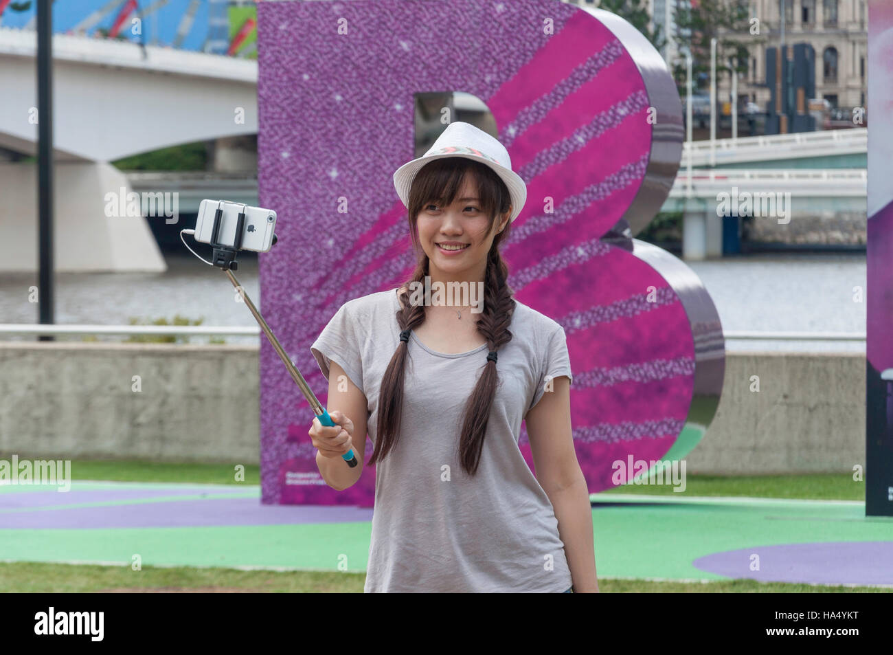 Junge Frau mit Selfie-Stick zum Fotografieren auf dem Iphone, South Bank Parklands, South Bank, Brisbane, Queensland, Australien Stockfoto