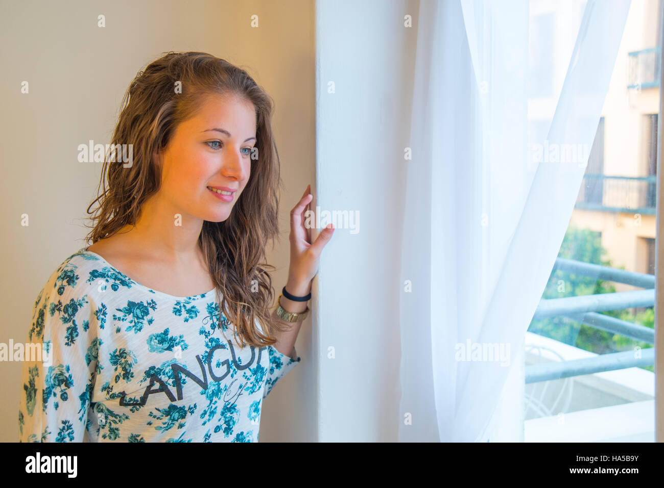 Junge Frau lächelnd und Blick durch das Fenster. Stockfoto