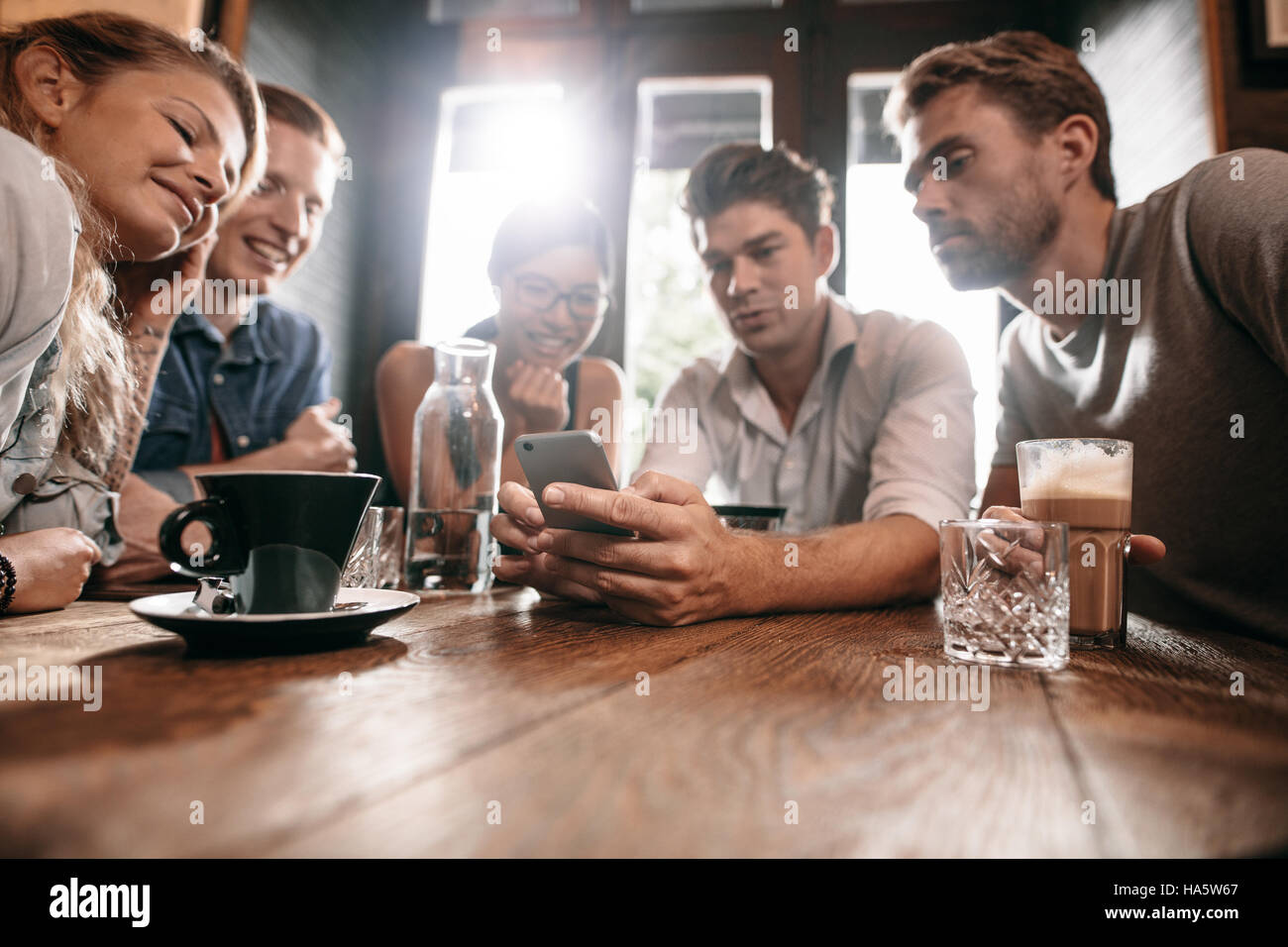 Gruppe von Freunden im Café und Smartphone betrachten. Mann zeigt etwas zu seinen Freunden zu sitzen. Stockfoto