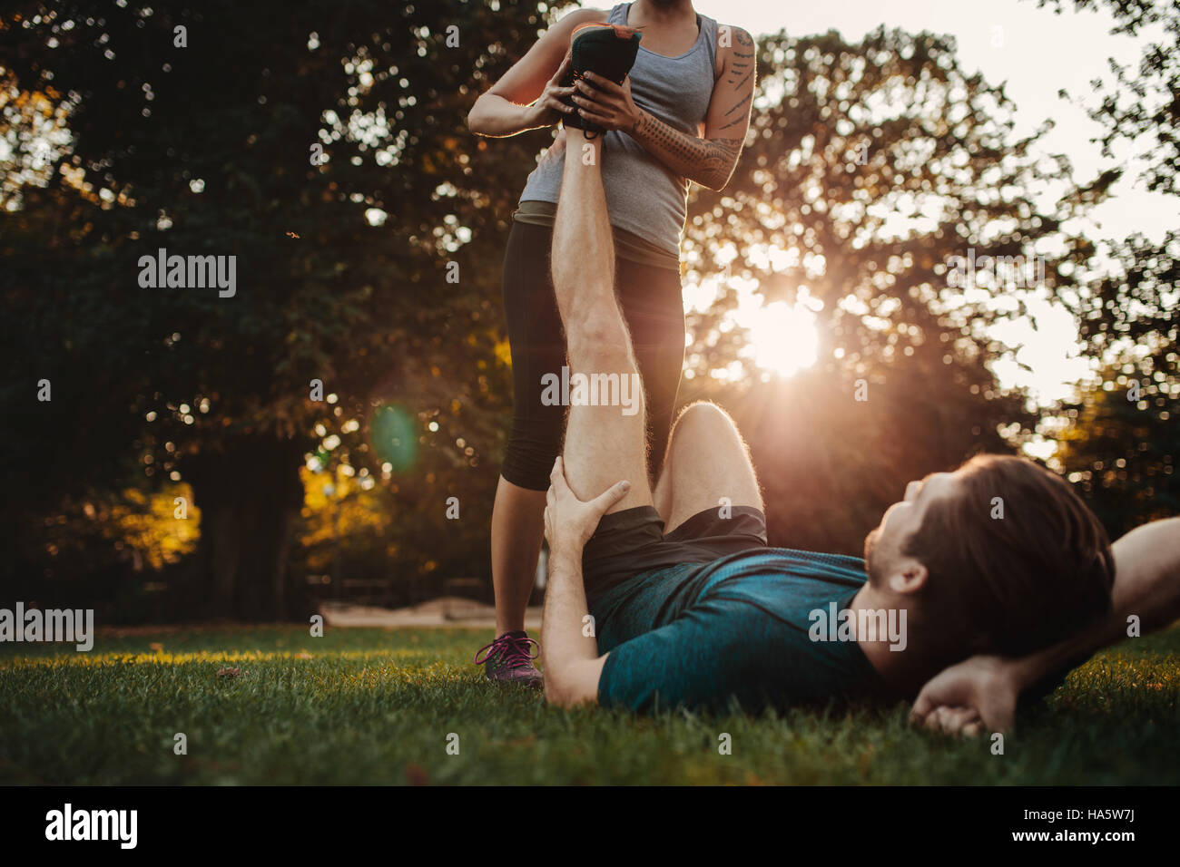 Junger Mann mit einem Stamm und gestreckt von weiblichen Trainer. Frau streckt das Bein Mannes, Muskelkrämpfe nach dem Sport Training. Stockfoto