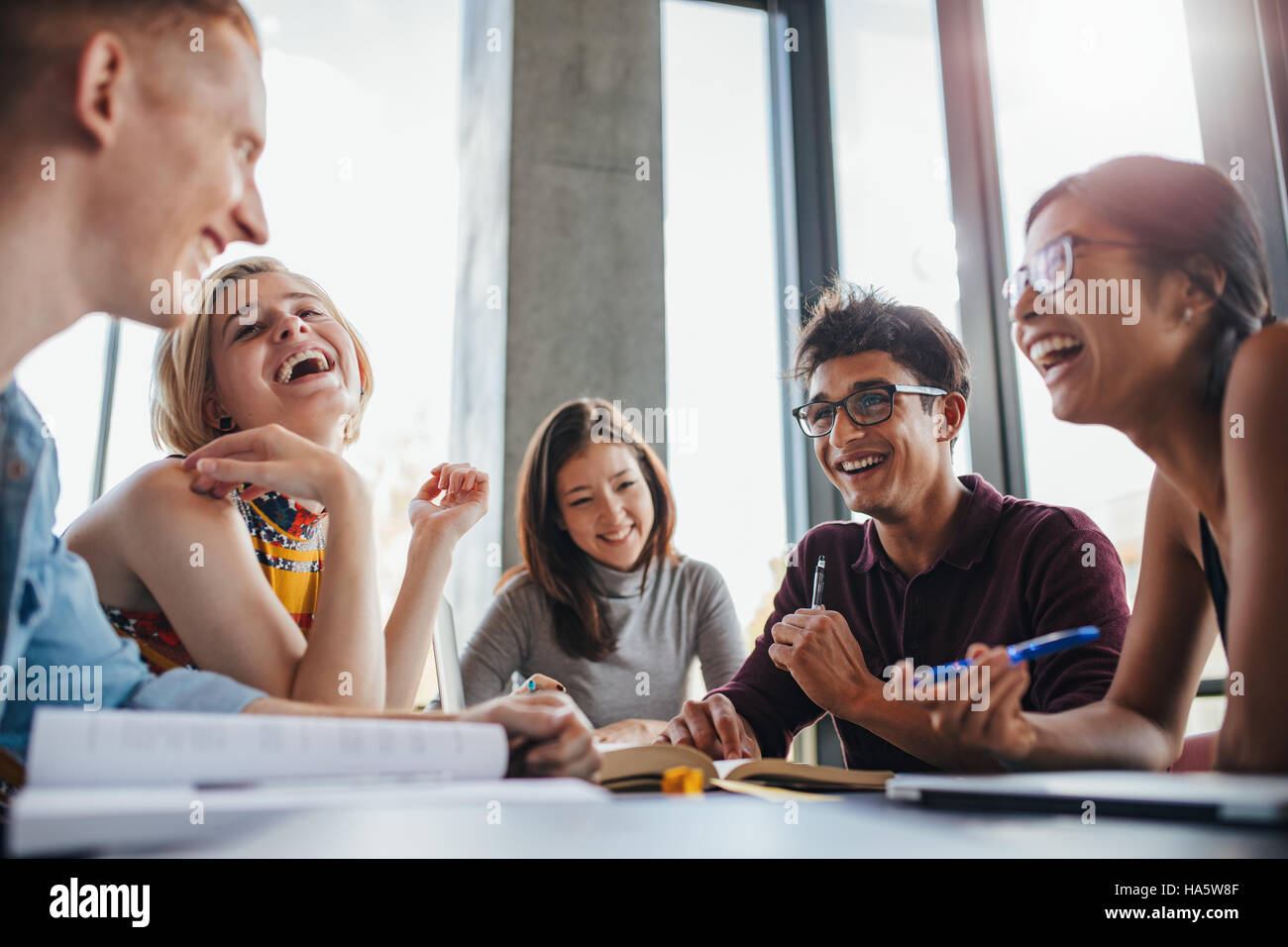 Multiethnische junge Leute am Tisch sitzen und Spaß beim Lernen für Klausuren zusammen. Gruppe von glücklichen jungen Studenten in Bibliothek. Stockfoto