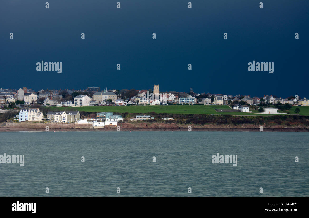 Deep Blue stürmischen Himmel über Milford Haven mit Sonnenlicht auf Kirche, Häuser und ein Patch der hellen grünen Gras über eine kühlere Meer Stockfoto