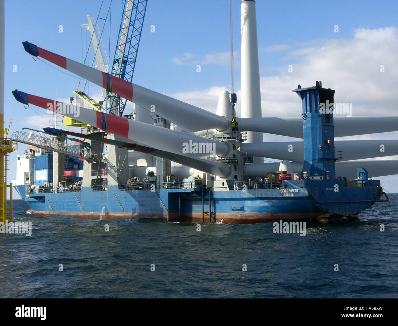 Diese Abbildung zeigt den detaillierten Installationsvorgang eines Rotorblatts einer Windturbine, das von einem Kran auf einen Offshore-Windkraftanlagenturm angehoben wird. Sie hebt die Komplexität der Offshore-Windenergieinfrastruktur und die Rolle der erneuerbaren Energien bei der Bekämpfung des Klimawandels hervor. Stockfoto