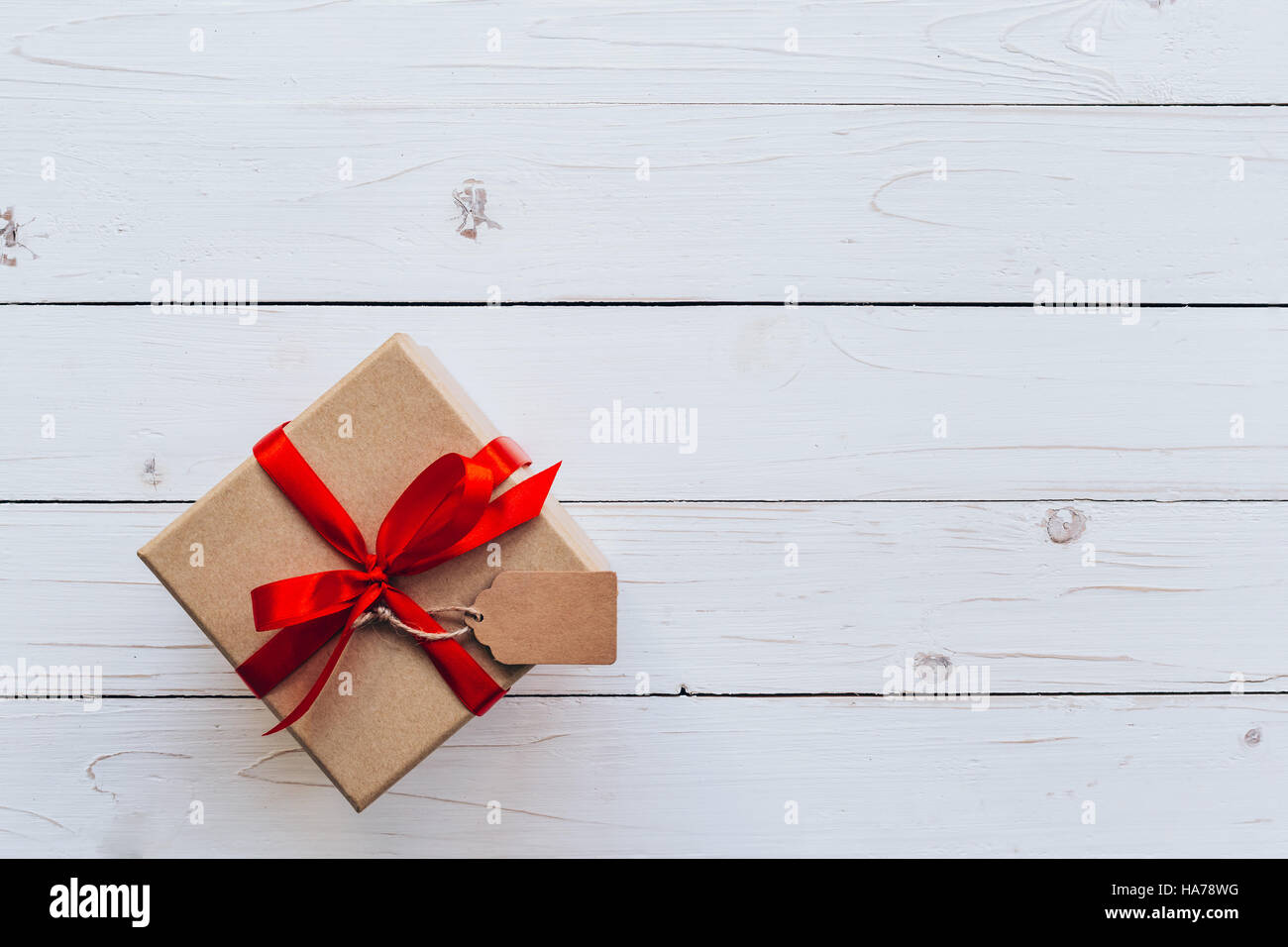 Oben braun Geschenkbox mit Tag auf Holzbrett Hintergrund. Geschenkbox mit rotem Band auf hölzernen weißen Hintergrund mit dem Raum. Stockfoto