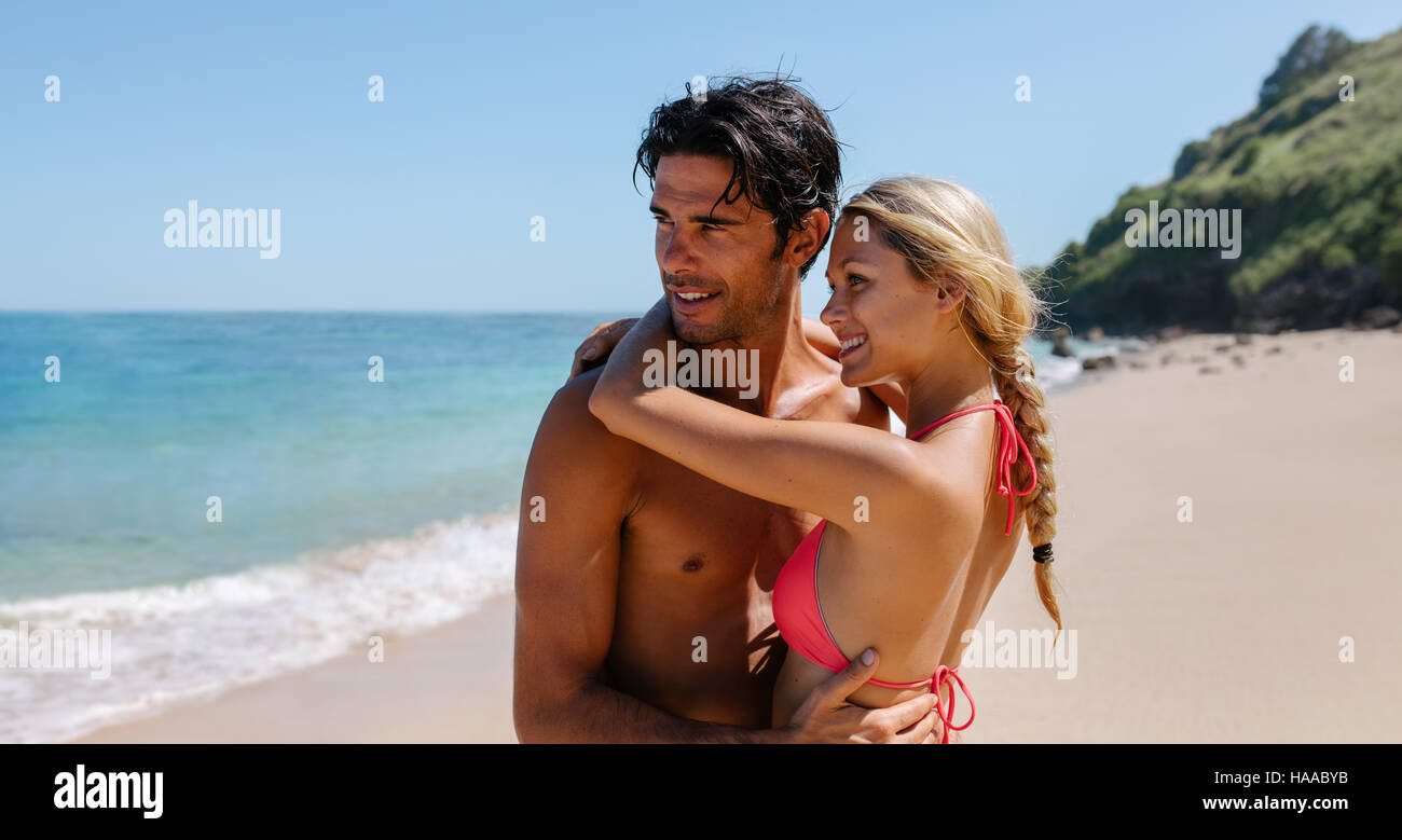 Liebevolle junge Paar umarmt am Strand und mit Blick auf das Meer. Romantische junge Paar zusammen am Meer Ufer wegsehen. Stockfoto
