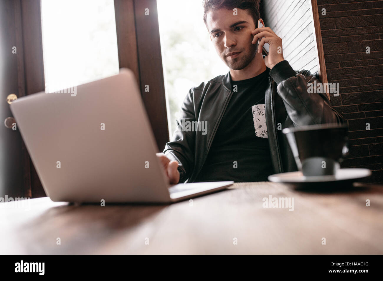 Gut aussehender Mann sitzen im Café-Tisch mit Tasse Kaffee mit Handy und Laptop. Stockfoto