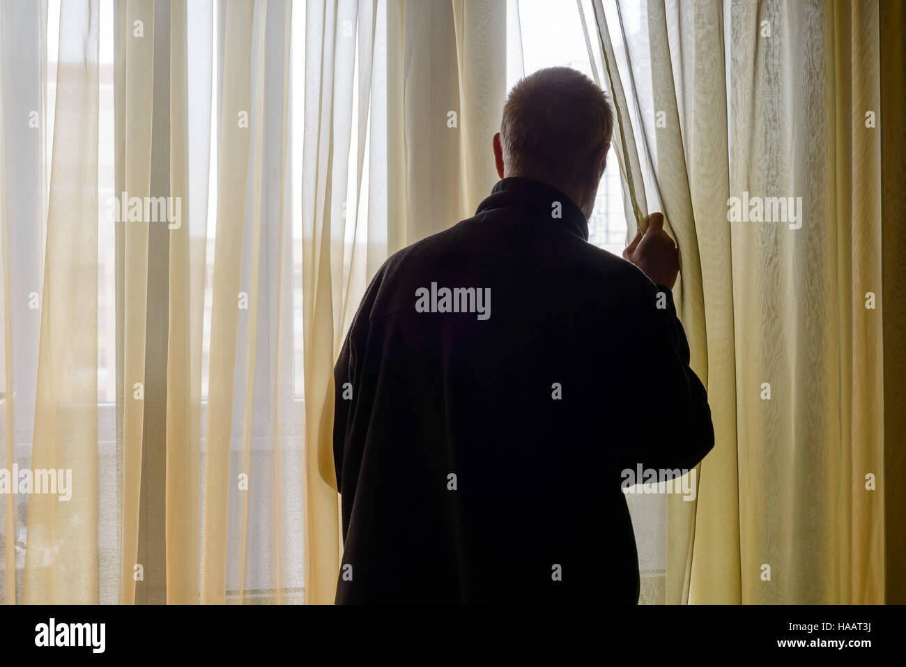 Ein Mann in Schwarz geht den Vorhang beiseite nach Trog die Fenster schauen Stockfoto