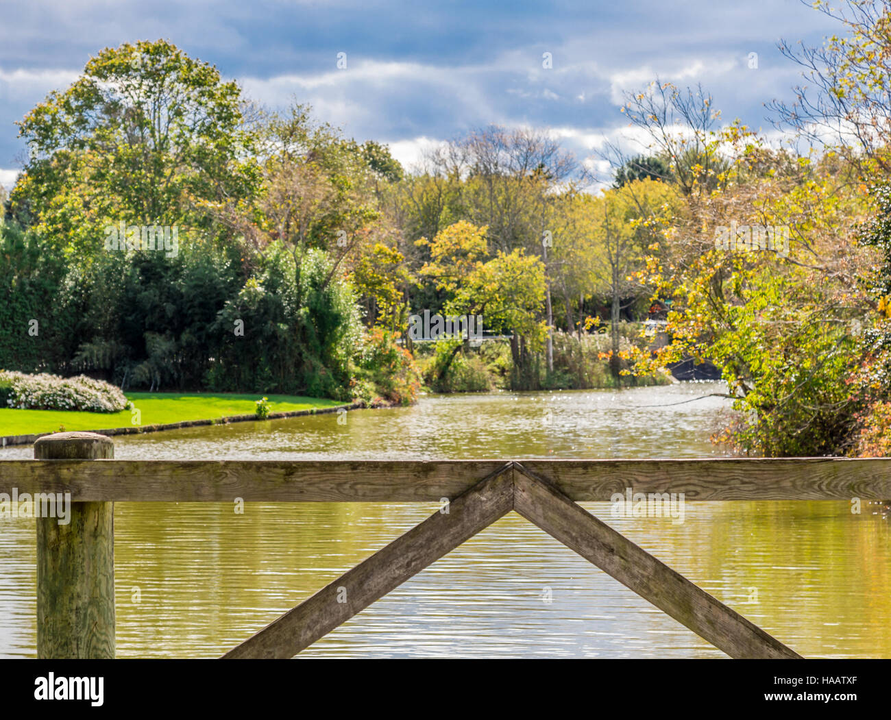 Blick von einer einfachen Brücke auf einen kleinen Körper des Wassers umgeben von Bäumen und Rasen Stockfoto
