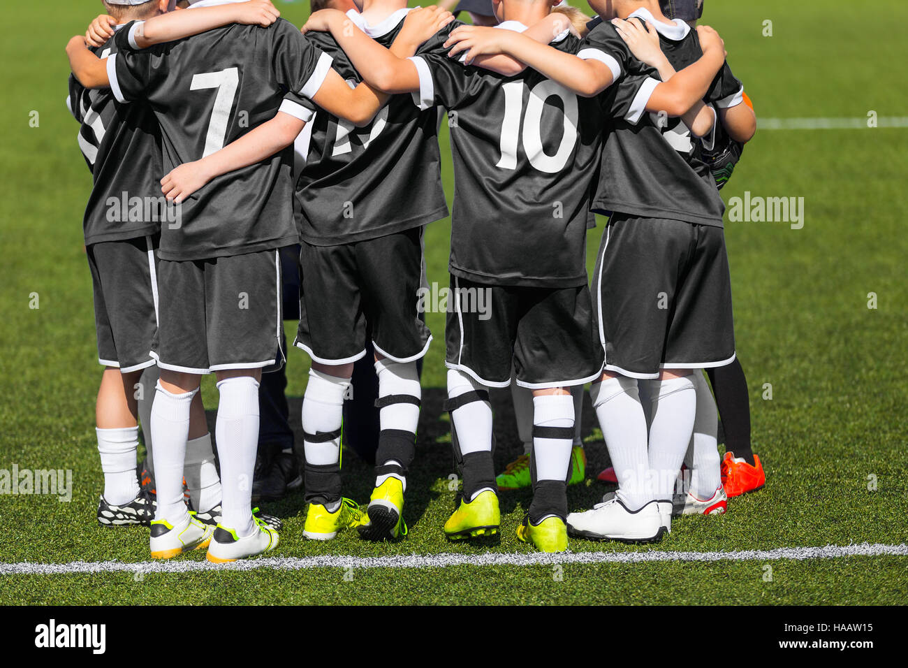 Jungen Fußball Fußball-Spieler in der schwarzen Sportswear. Junge Sportmannschaft mit Fußball-Trainer. Aufmunternde Worte mit Trainer vor dem Endspiel. Fußballschule Stockfoto