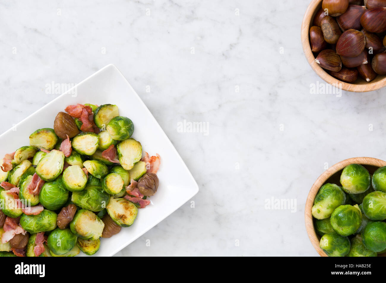 Rosenkohl mit Kastanien und Speck auf weißem Marmor Stockfoto