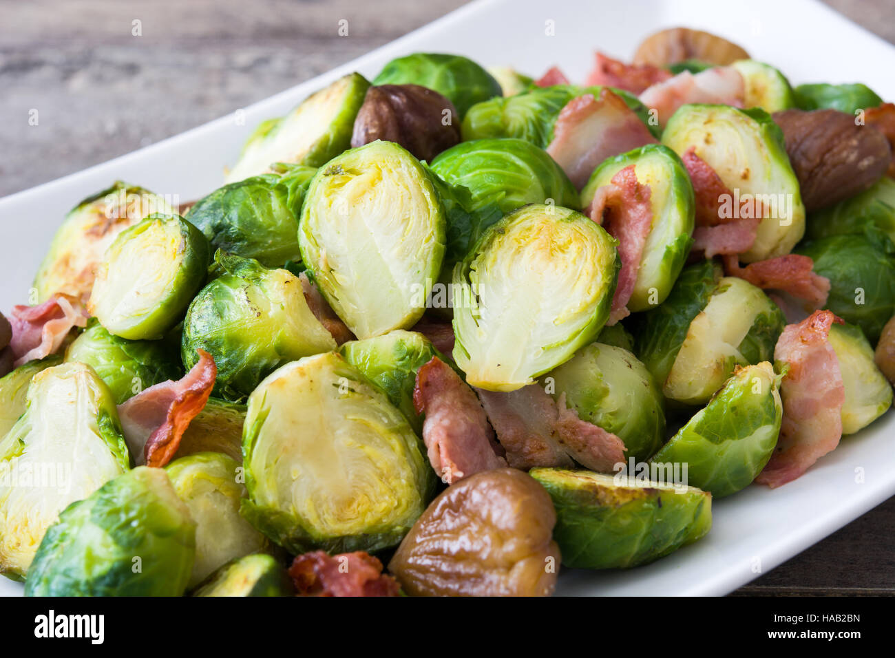 Rosenkohl mit Kastanien und Speck auf hölzernen Hintergrund Stockfoto