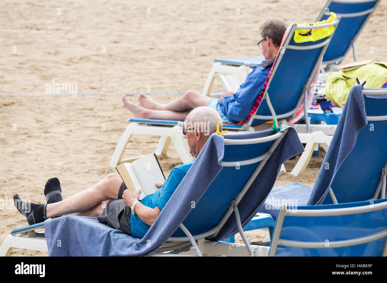 Reife Männer lesen Bücher am Strand in Spanien Stockfoto