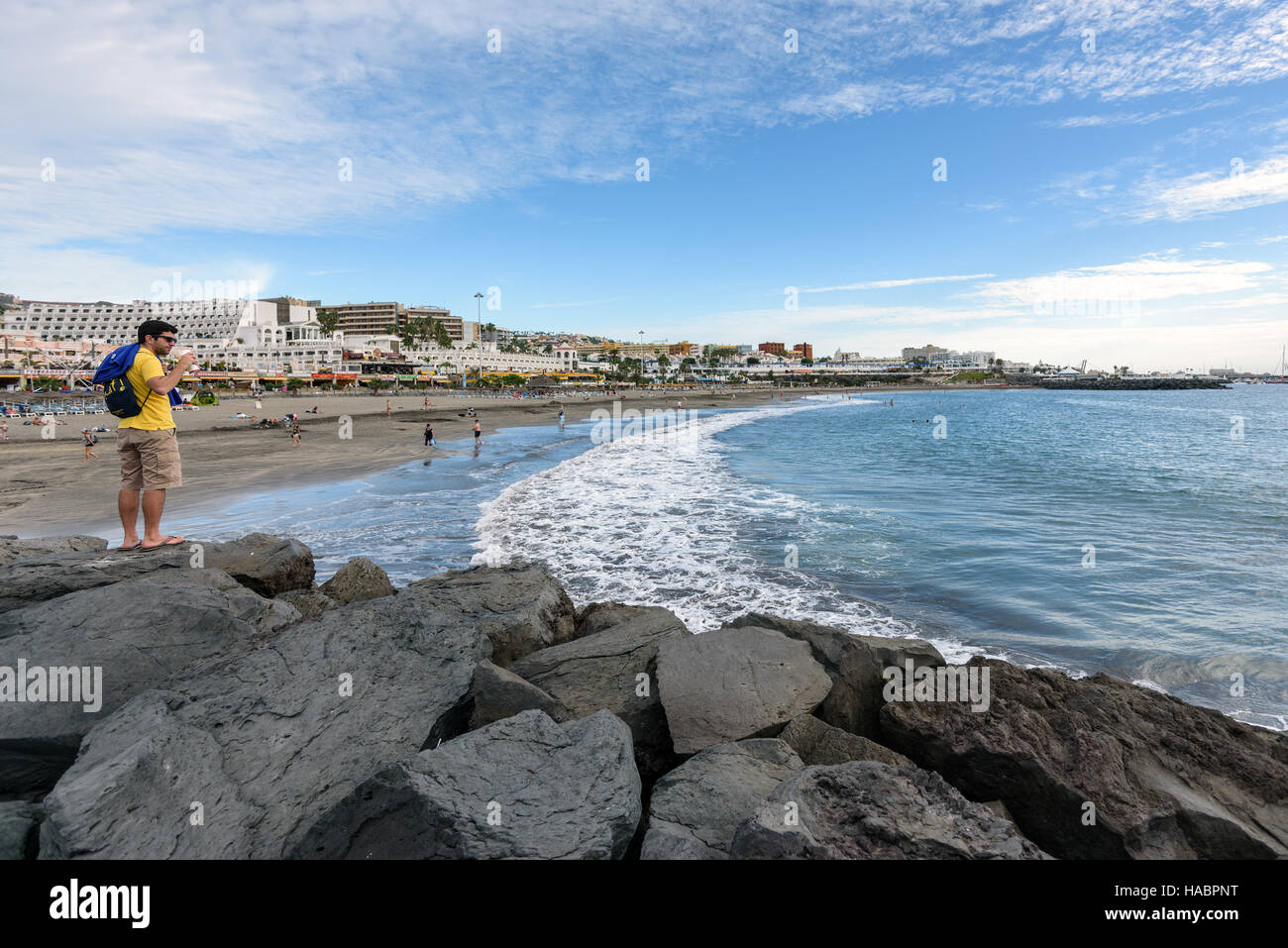 Mann im gelben T-shirt bleibt auf Steinen in der Nähe von schwarzen Sand Strand von Adeje Stadt auf der Insel Teneriffa, Spanien Stockfoto
