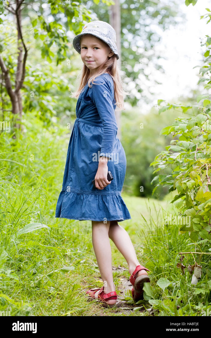kleines Mädchen im blauen Kleid auf grünen Sommer Hintergrund stehend Stockfoto