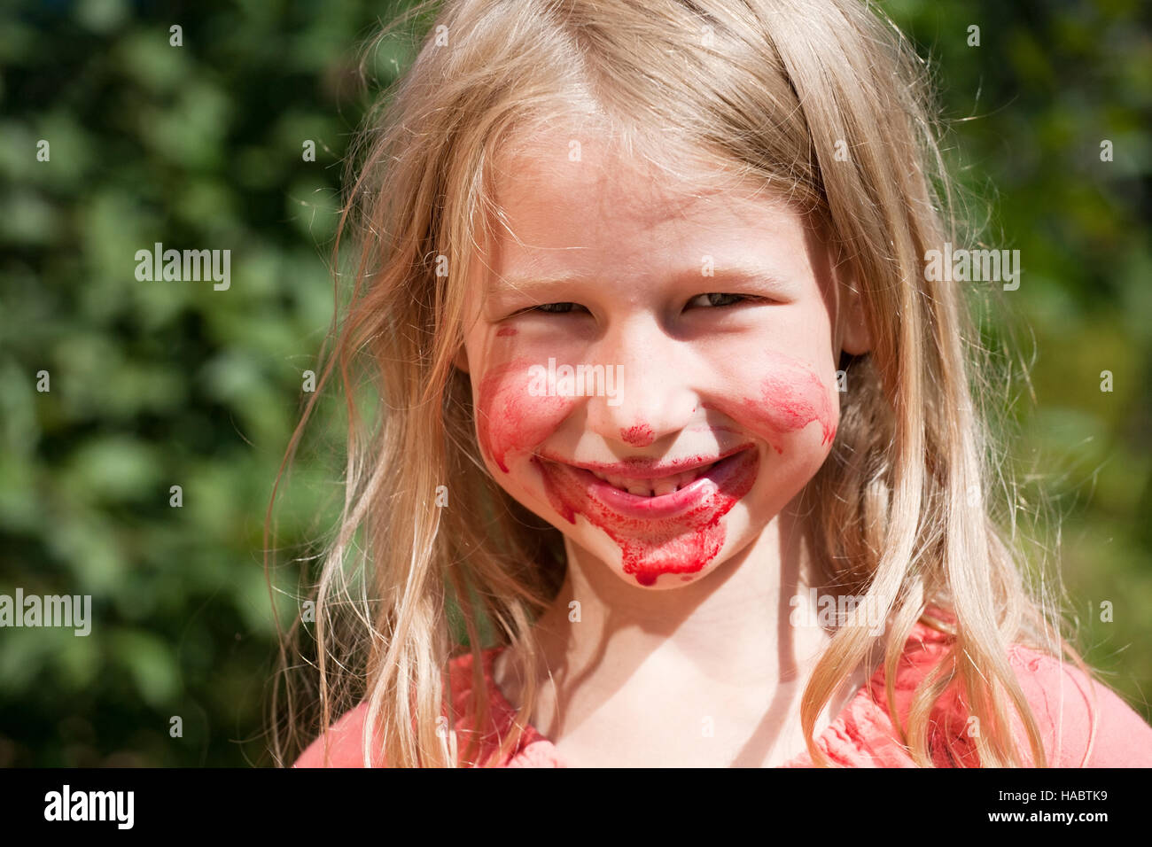 lustig lächelndes Mädchen mit roten Saft auf Wangen und Kinn Stockfoto