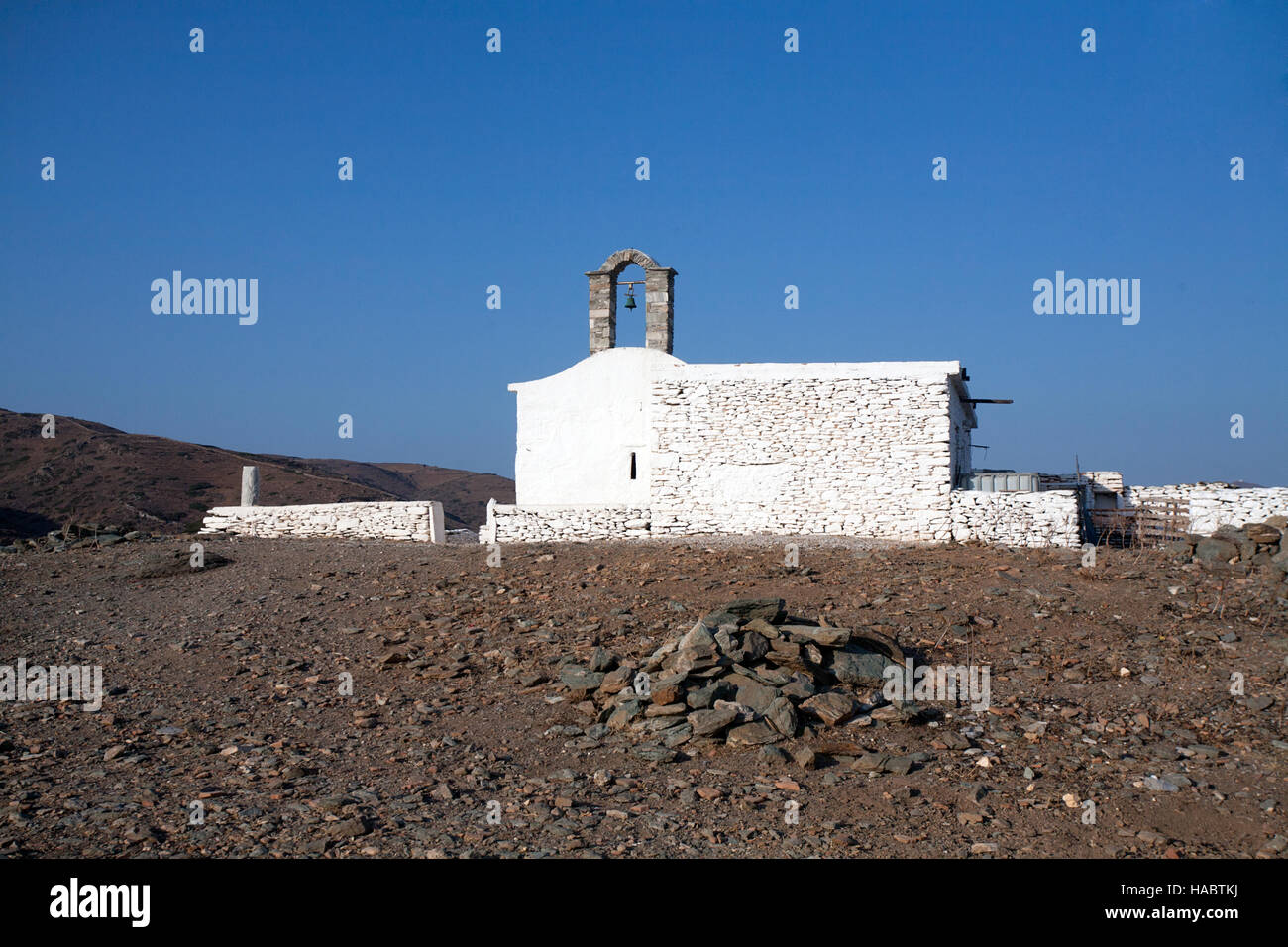 kleine griechische weiße Kirche mit Glockenturm auf steinigen Landschaft und strahlend blauem Himmelshintergrund Stockfoto