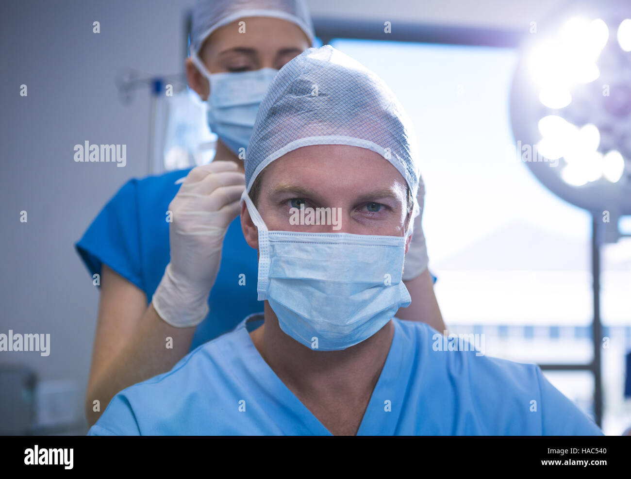 Krankenschwester in OP-Maske an ihre Kollegen im Betrieb Theater binden helfen Stockfoto