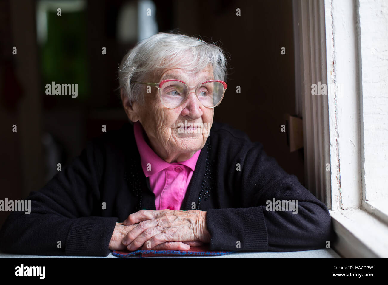 Eine ältere Frau sitzt am Fenster. Stockfoto
