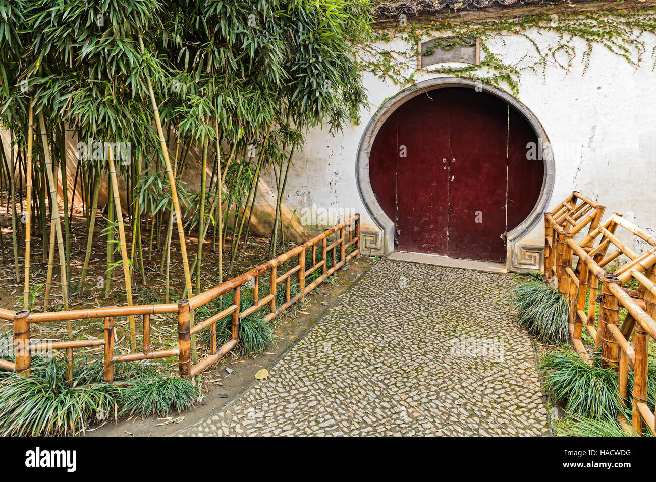 Traditionelle chinesische Gartenanlage - shut weiße Umfassungsmauer mit Schlüsselloch Holztür von kleinen Bambus-Pflanzen und gehen weg mit Cobbleston verziert Stockfoto