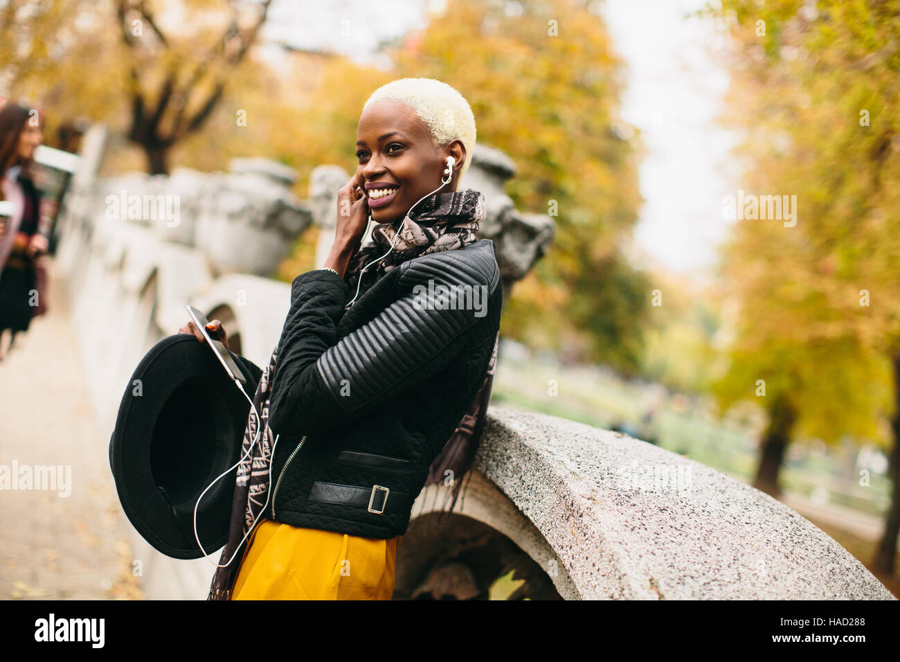 Moderne junge afroamerikanische Frau posiert mit Kaffee zum mitnehmen und Outdoor-Handy Stockfoto