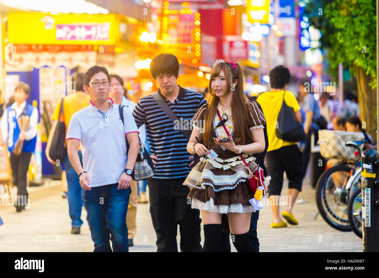 Junge japanische Mädchen in Französisch Maid Outfit anziehen der männlichen Kunden auf dem Bürgersteig um japanische Maid Café Restaurant betreten Stockfoto