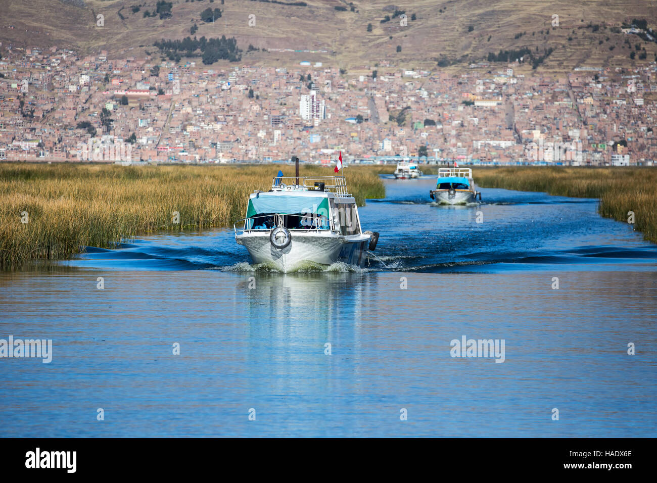 Ausflugsboote auf dem Titicacasee flankiert von Totora-Schilf-Felder, Stadt Puno im Hintergrund, Puno, Peru Stockfoto