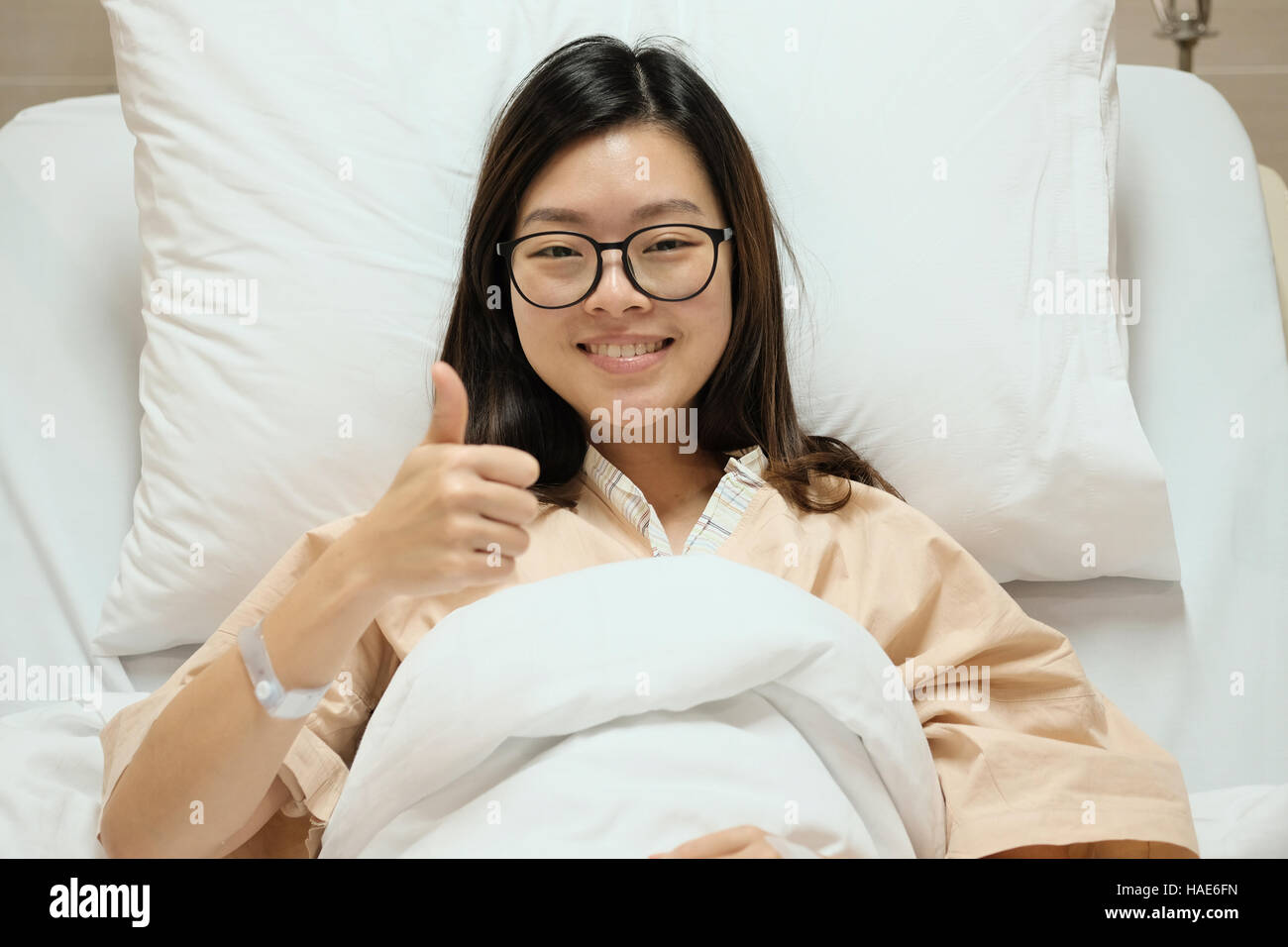 Schöne Asiatin Patienten Daumen hoch und Lächeln auf Krankenhaus Eintritt Bett, medizinischen oder gesundheitlichen Konzept Stockfoto