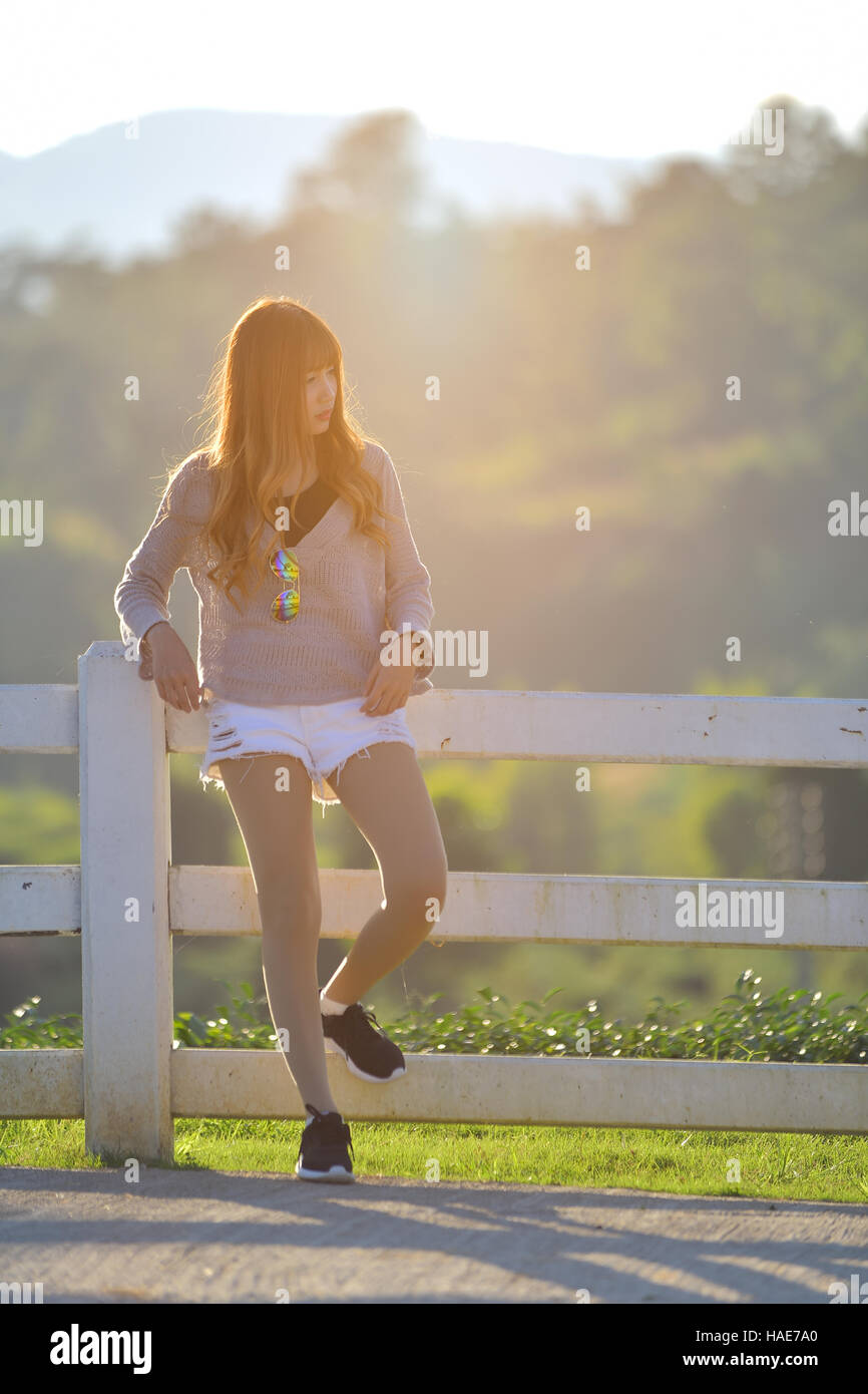 Junge asiatische Frau Kleid in Casual und Jeans, stehend an einem Zaun auf einer Ranch in warmen Ton Stockfoto