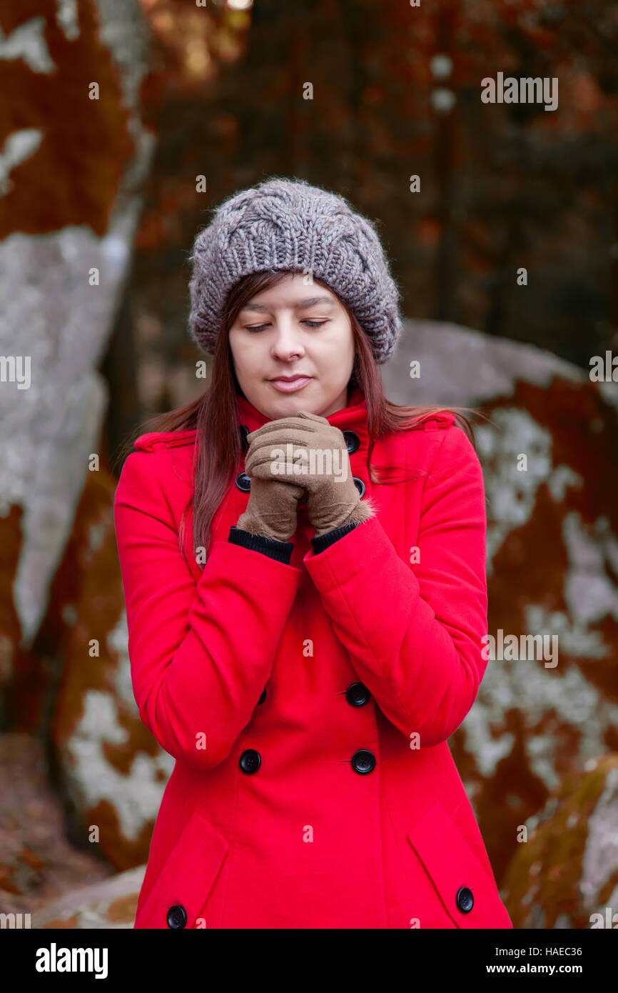Junge Frau, die zitternd vor Kälte auf einen Wald tragen einen roten Mantel, eine Mütze und Handschuhe im winter Stockfoto