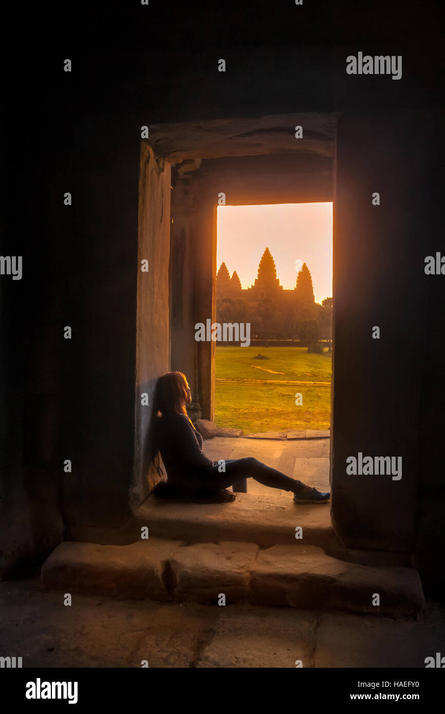Eine junge Frau wacht die Sonne aufgehen über Angkor Wat aus einer Tür in einer der kleineren Tempel. Stockfoto