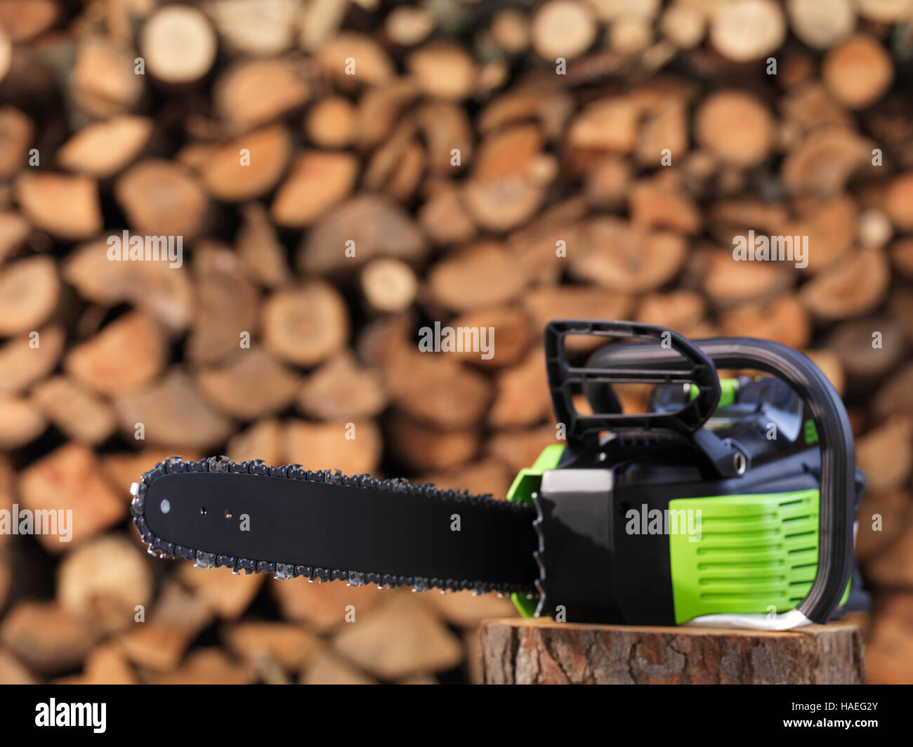 Elektrische Cordless Batterie betriebene Kettensäge vor gestapelten Brennholz im Hintergrund Stockfoto