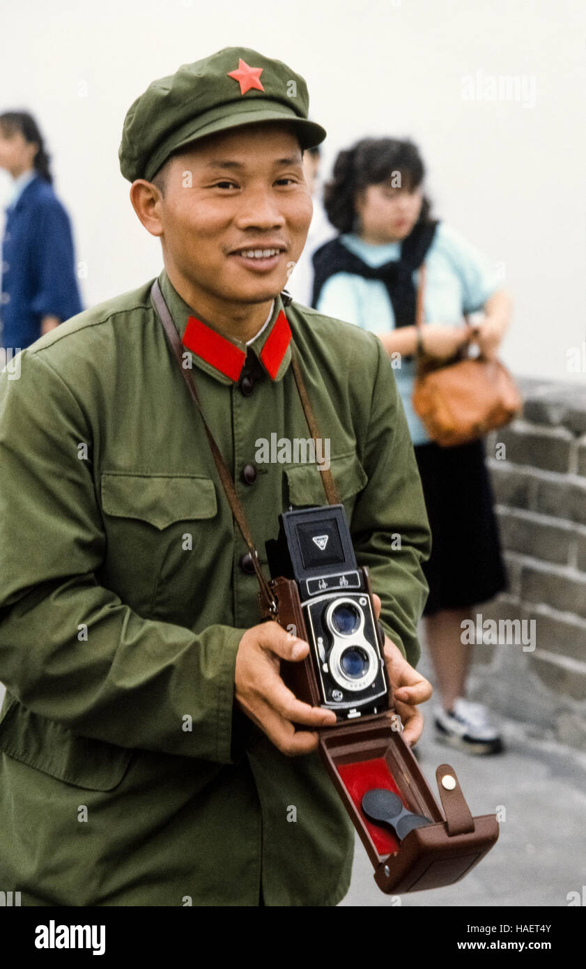 Ein lächelnder jungen chinesischer Soldaten in seiner einfachen olivgrün Armee uniform der Great Wall Of China in den 1980er Jahren besucht und Sehenswürdigkeit des Landes mit einer altmodischen Twin Lens Reflex Filmkamera fotografiert. Stockfoto