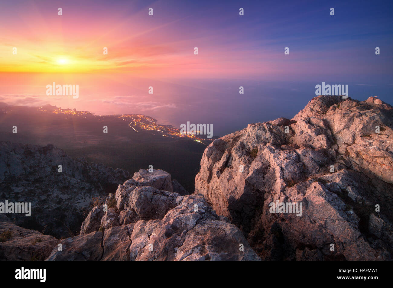 Blick vom Gipfel auf Felsen, Citylights, bunten Himmel und Meer am Abend. Berglandschaft bei Sonnenuntergang. Stockfoto