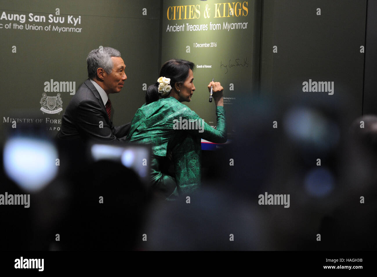 Myanmar, Singapur. 1. Dezember 2016. Myanmars State Counselor Aung San Suu Kyi (R), begleitet von Singapurs Premierminister Lee Hsien Loong, unterschreibt ihr Name bei der Eröffnungsfeier der Ausstellung "Städte und Könige: alte Schätze aus Myanmar" in Singapurs asiatischen Zivilisationen Museum, 1. Dezember 2016. Myanmars Zustand Ratgeber Aung San Suu Kyi nahmen an der Eröffnungsfeier der den "Städten und Königen: alte Schätze aus Myanmar" am zweiten Tag ihrer dreitägigen offiziellen Besuch nach Singapur. Bildnachweis: Xinhua/Alamy Live-Nachrichten Stockfoto