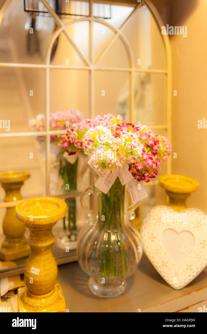 Eine Vase mit Blumen auf einem Regal neben einem Spiegel mit Kerzen. Stockfoto