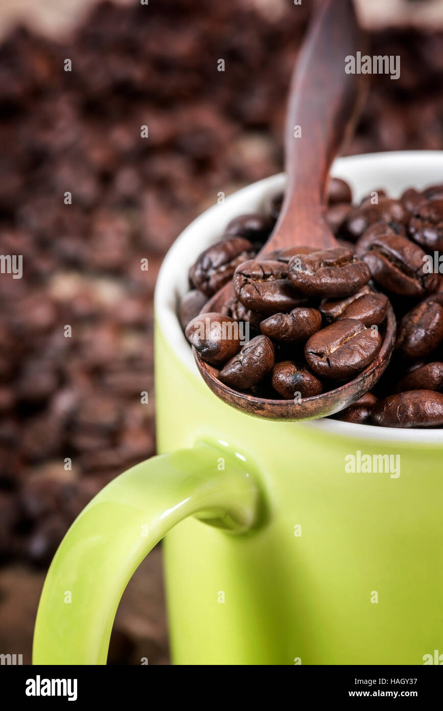 Kaffeebohnen in Holzlöffel setzen auf grüne Tasse mit Kaffeebohnen Hintergrund. Stockfoto
