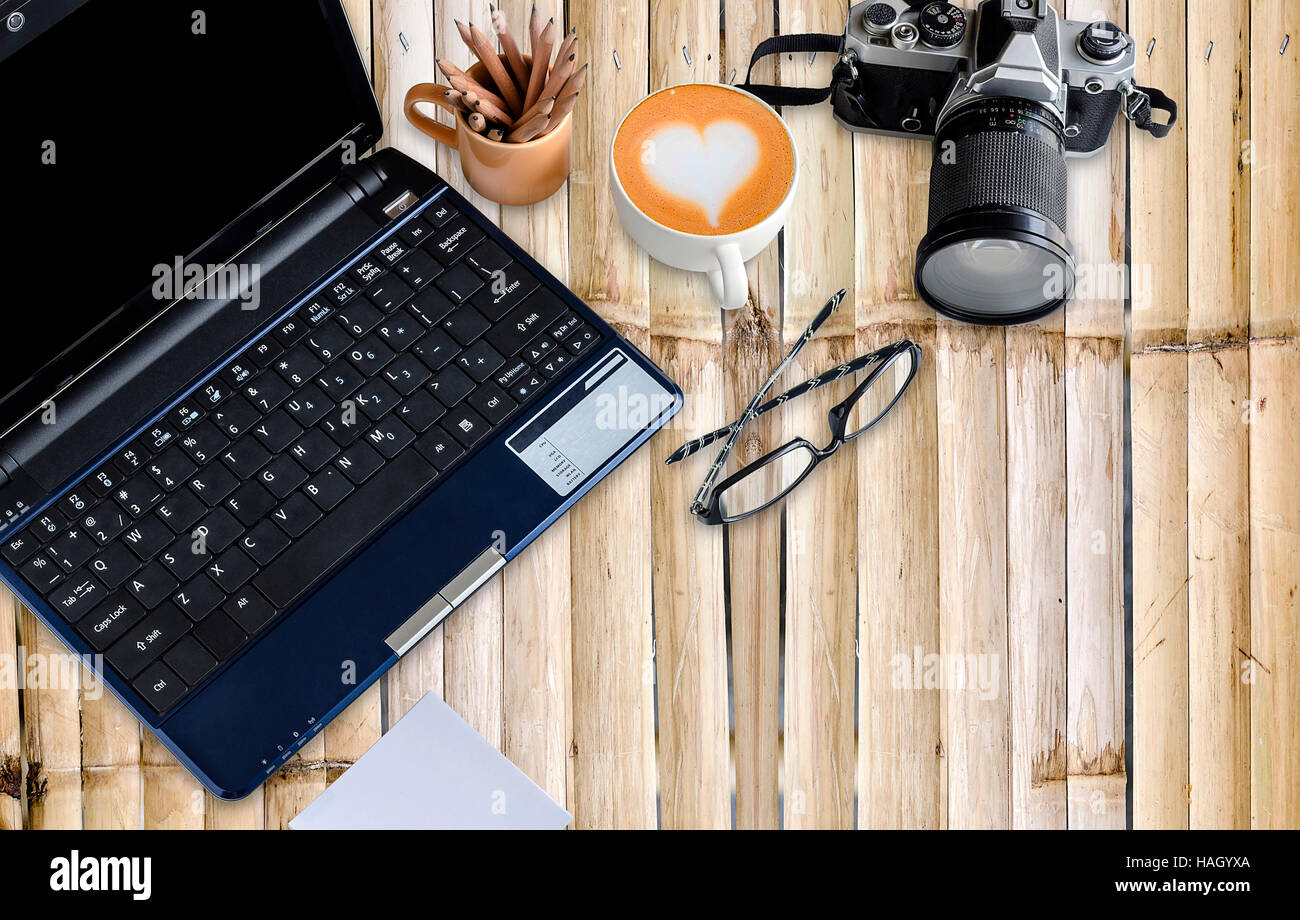 Bambus-Desktop mit Notebook, Vintage-Kamera, Tasse Kaffee und Brillen. Stockfoto