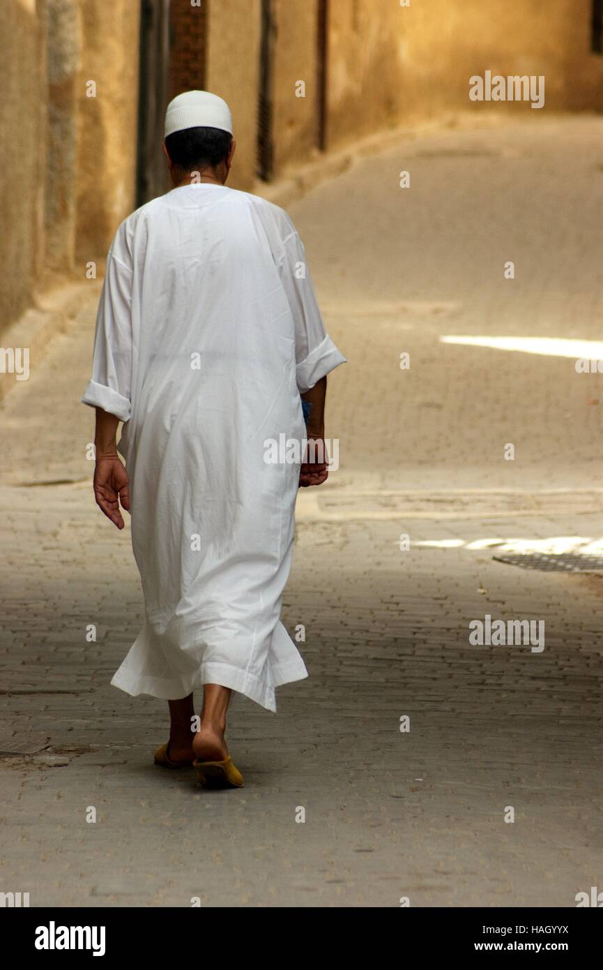 Ein muslimischer Mann in traditioneller weißer Djellaba wandert in einer Gasse in der Altstadt von Fez, Marokko. Stockfoto