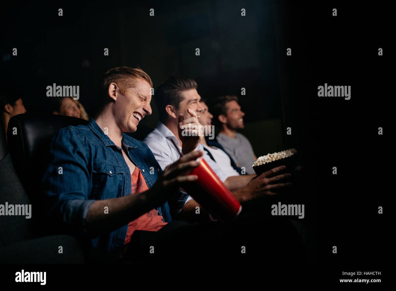 Junger Mann mit Freunden im Kinosaal Film ansehen und lachen. Gruppe von Menschen Film im Theater. Stockfoto
