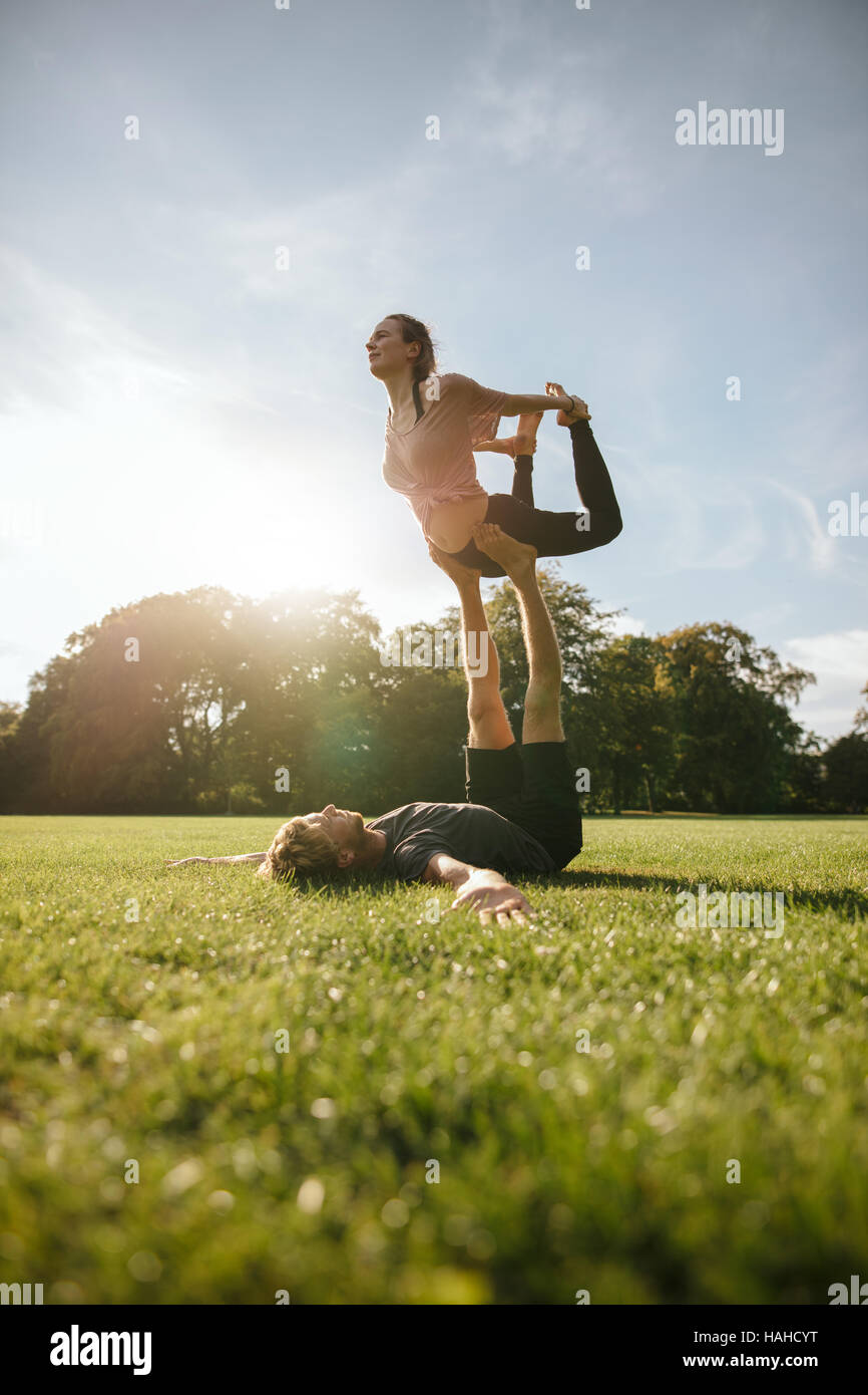 Starke junge Paar paar Yoga im Freien im Park machen. Mann heben und balancing Frau im Park. AcroYoga Training an einem sonnigen Morgen. Stockfoto