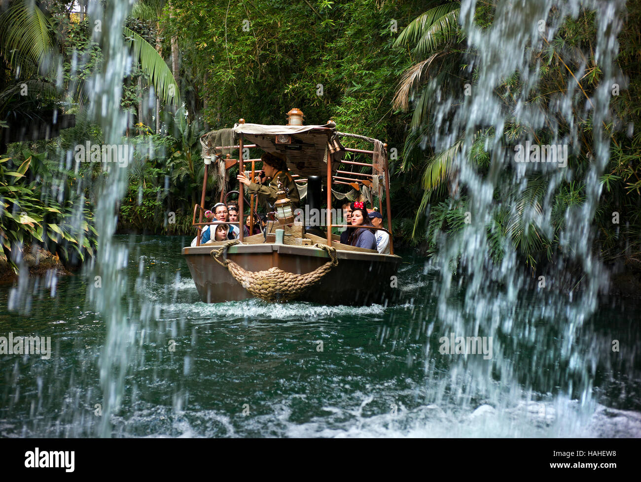 Besucher von Disneyland fahren auf der Jungle Cruise in der Nähe eines Wasserfalls oder auf der Rückseite des Wassers. Stockfoto
