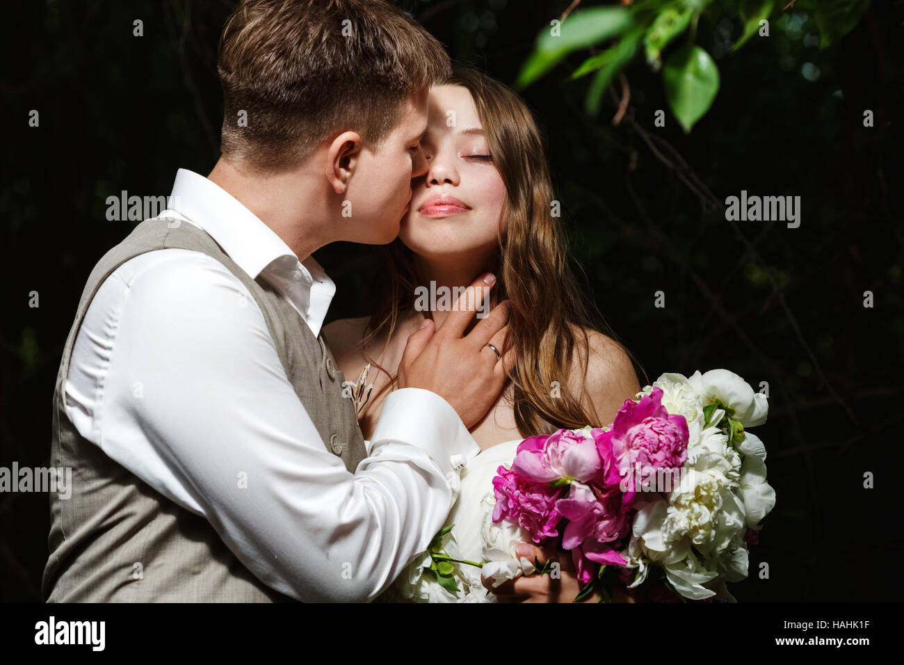 Brautpaar küssen im Park, Braut hält Blumen Stockfoto
