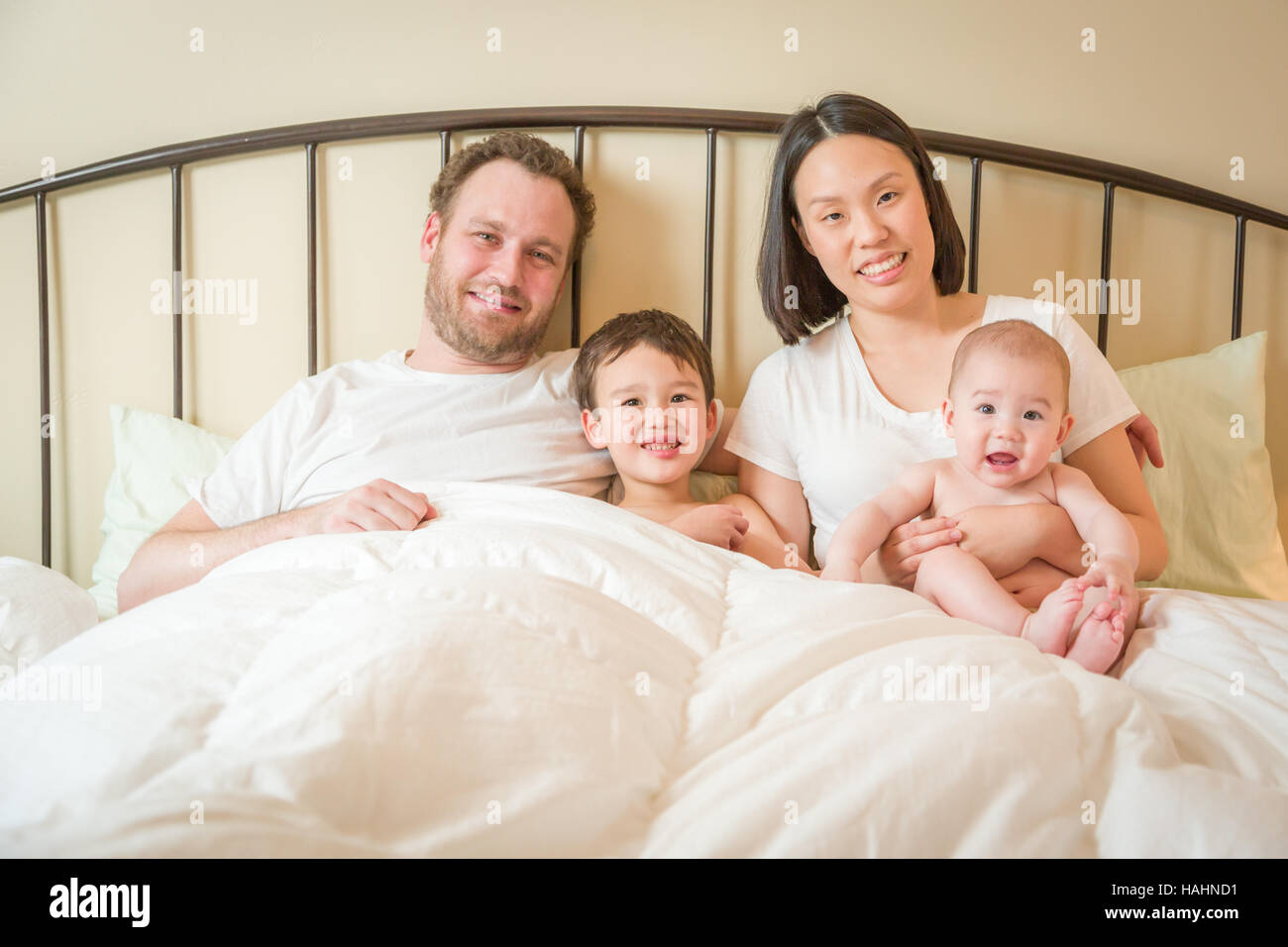 Junge Mischlinge chinesische und kaukasischen jungen Verlegung In mit ihrem Vater und Mutter Bett. Stockfoto