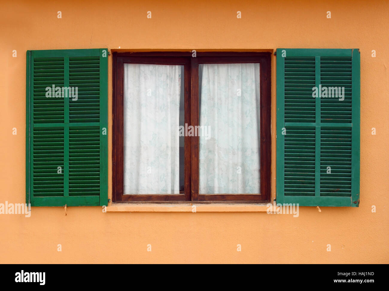 grüne Fensterläden auf gelbe Hausfassade eröffnet Stockfoto