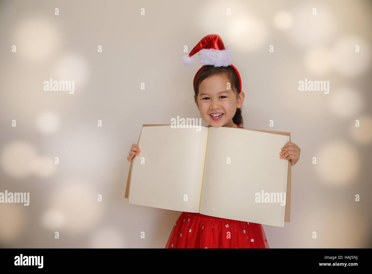 Niedliche kleine Santa Mädchen hält Kopie Raum Buch mit Lichterkette Tonen Hintergrund Stockfoto