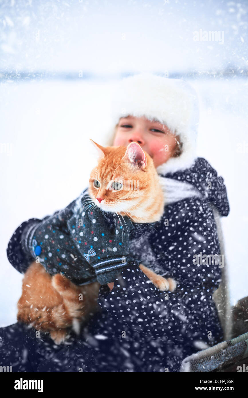 Kleines Mädchen hält eine rote Katze in ihren Händen sitzen in einem Schlitten im Winter. Stockfoto