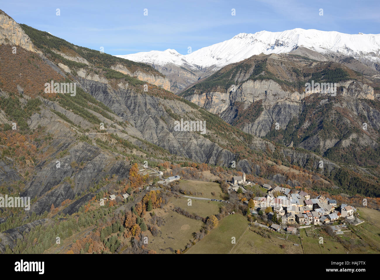 LUFTAUFNAHME. Mittelalterliches Dorf auf einem Hügel in einer Landschaft aus Badlands und schneebedeckten Gipfeln. Chateauneuf d'Entraunes, Alpes-Maritimes, Frankreich. Stockfoto