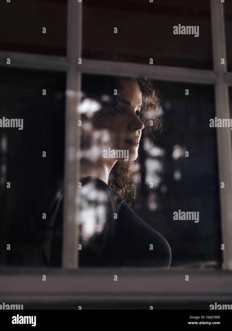 Führerschein und Drucke bei MaximImages.com - wunderschöne Frau hinter Reflexionen auf dem Fensterglas bei schwachem Licht Stockfoto